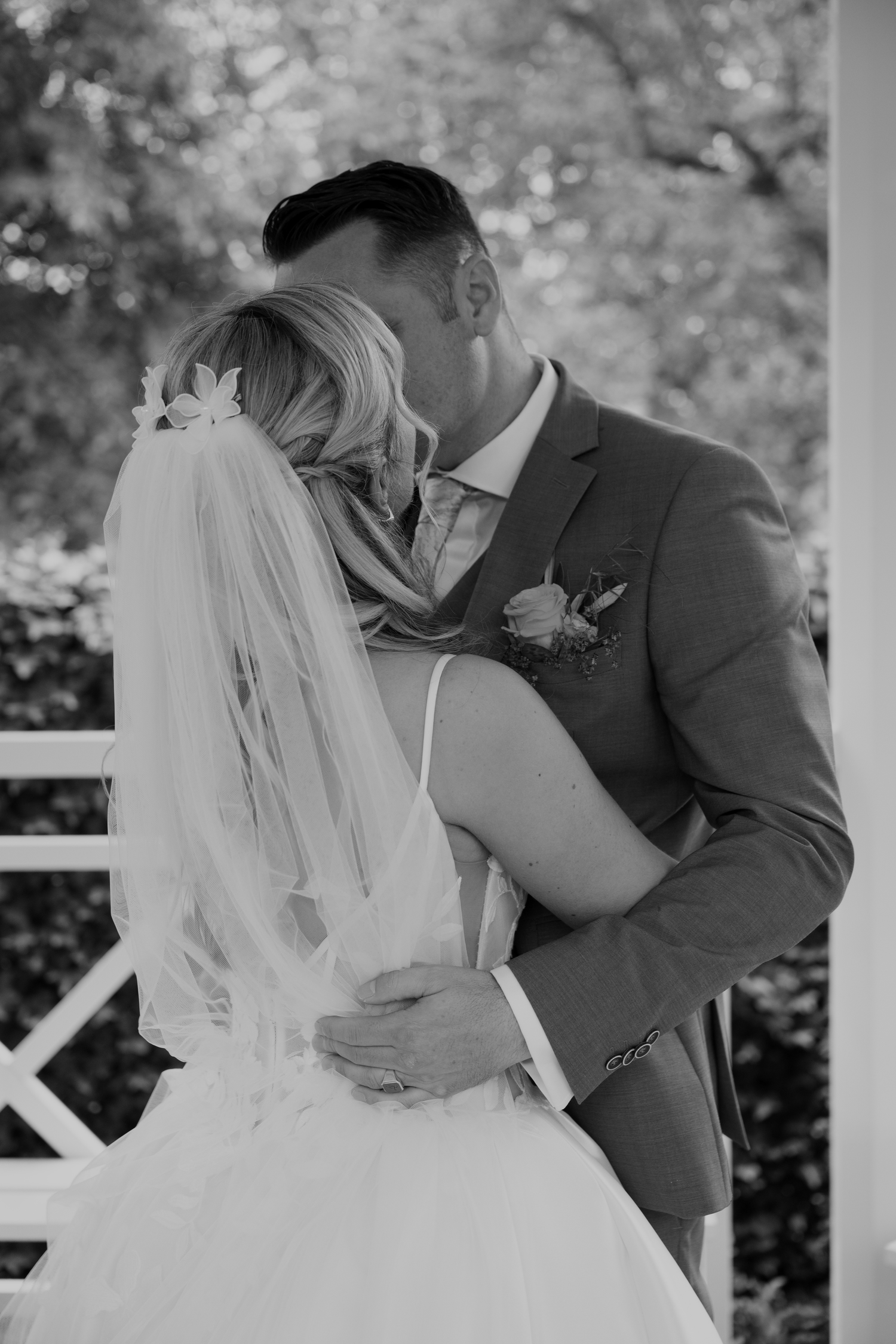 Black and white photo of a bride and groom sharing a romantic kiss, bride wearing veil with floral crown.
