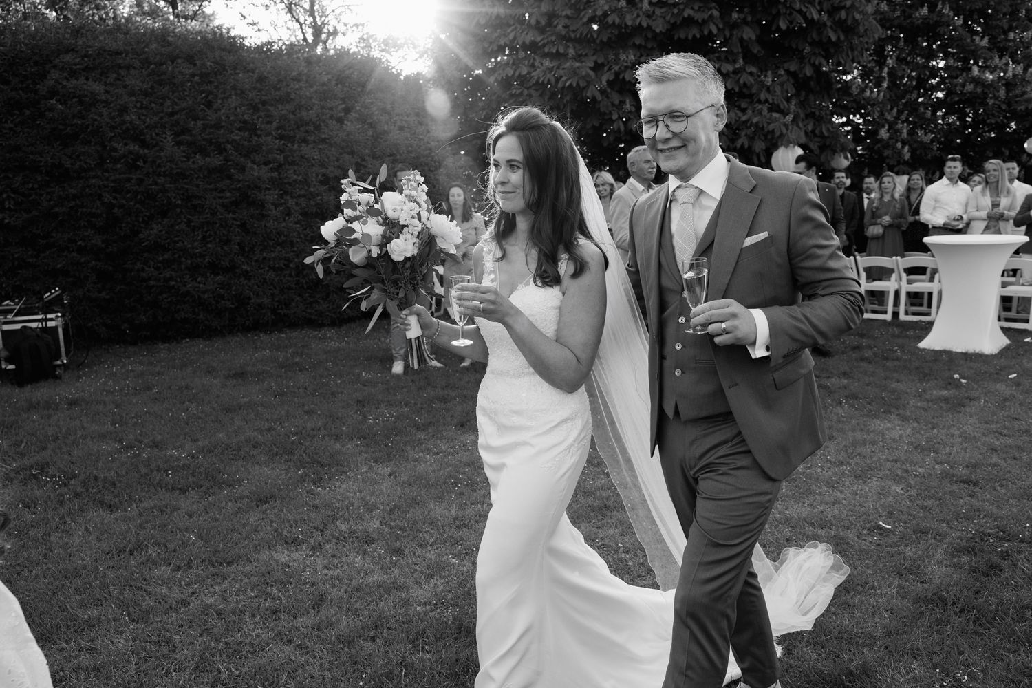 Black and white photo of a bride and groom walking together outdoors after their wedding ceremony.