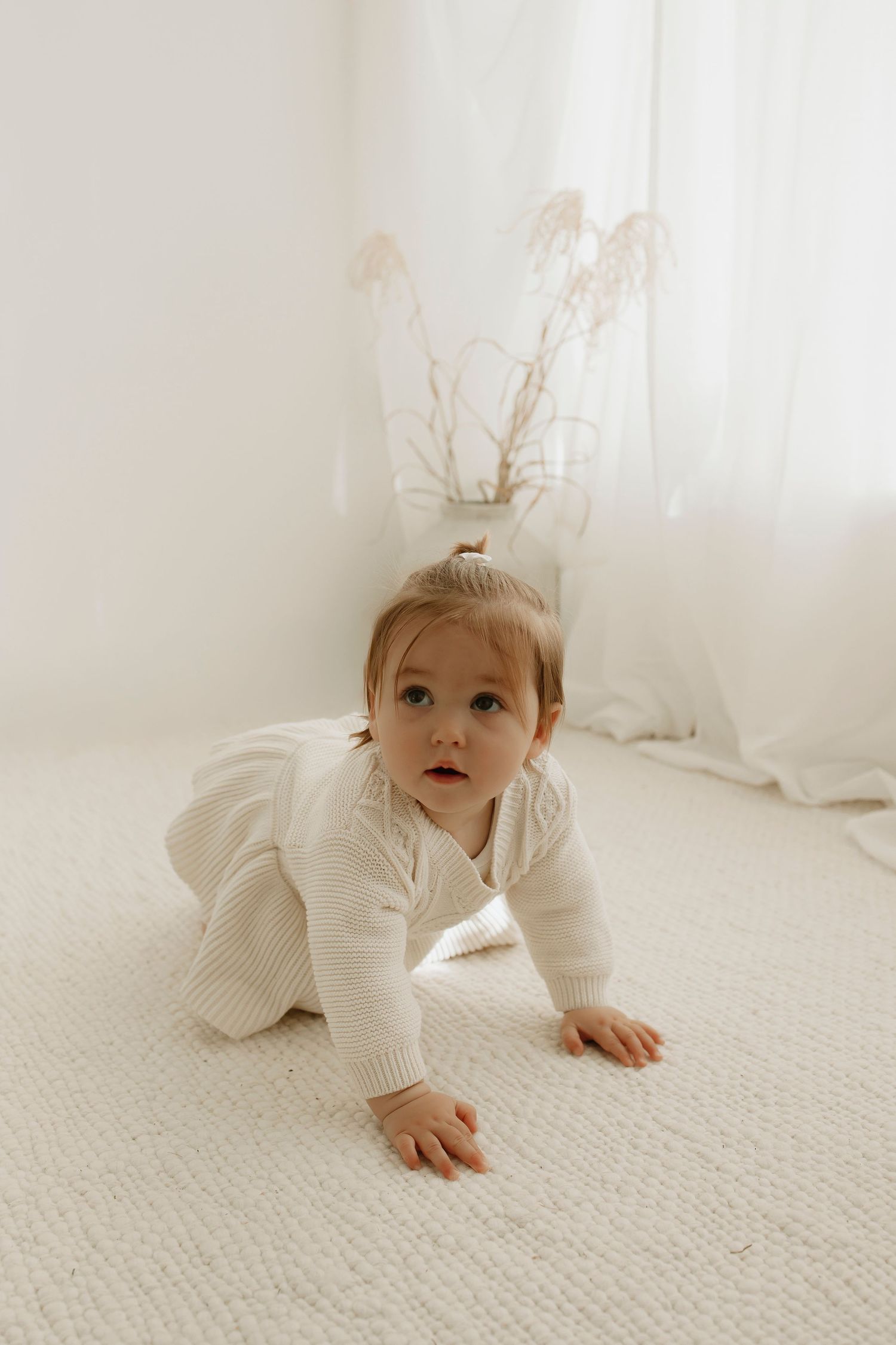 Baby in white outfit crawling on textured white carpet.