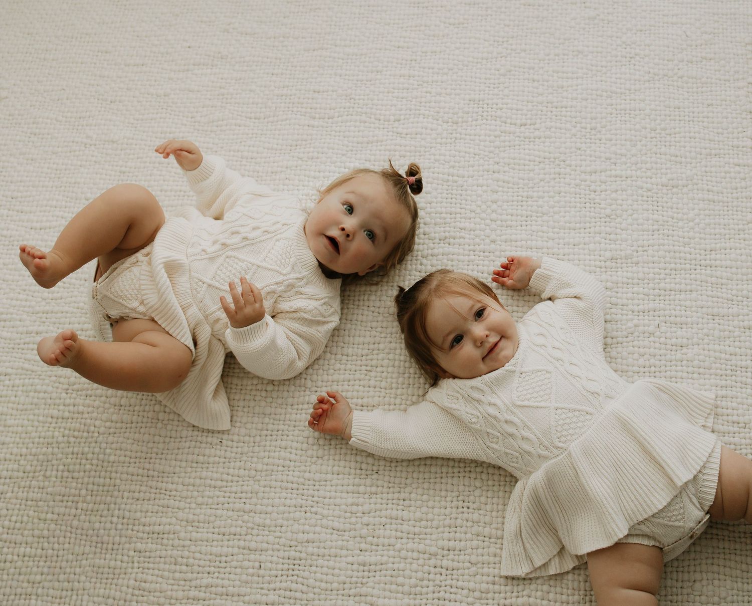 Baby in white outfit rolling playfully on beige carpet.