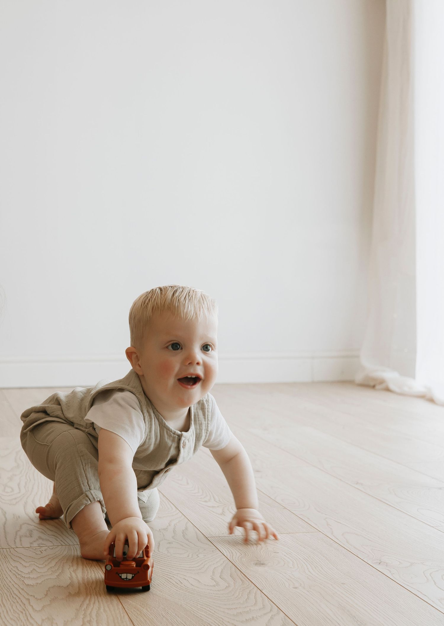 Baby in tan outfit crawling on white wooden floor.