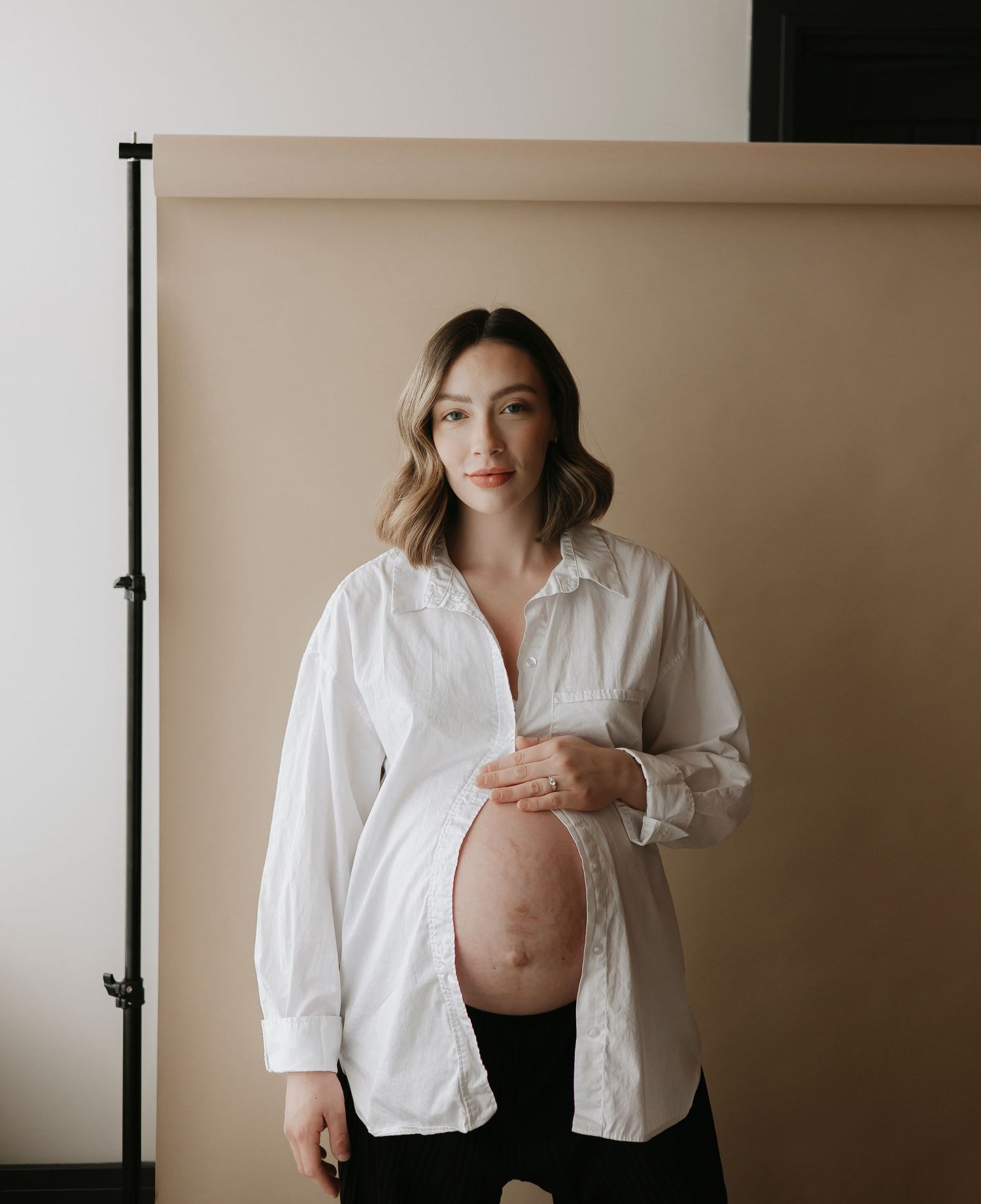 Artistic maternity photos showing a pregnant figure in a white button down shirt.