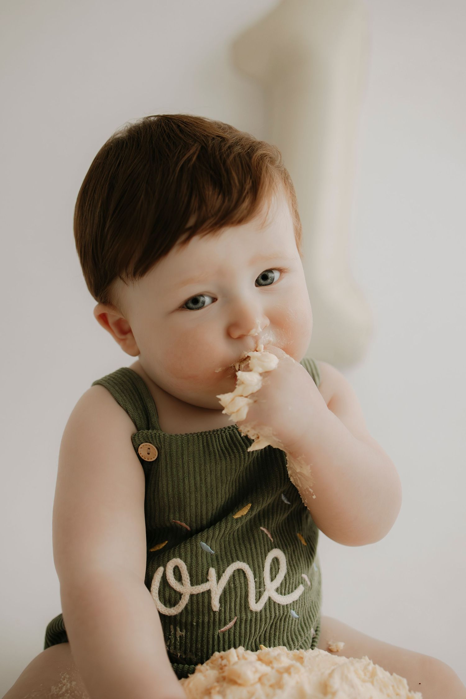 Baby in green tank top enjoying cake smash with frosting on face.