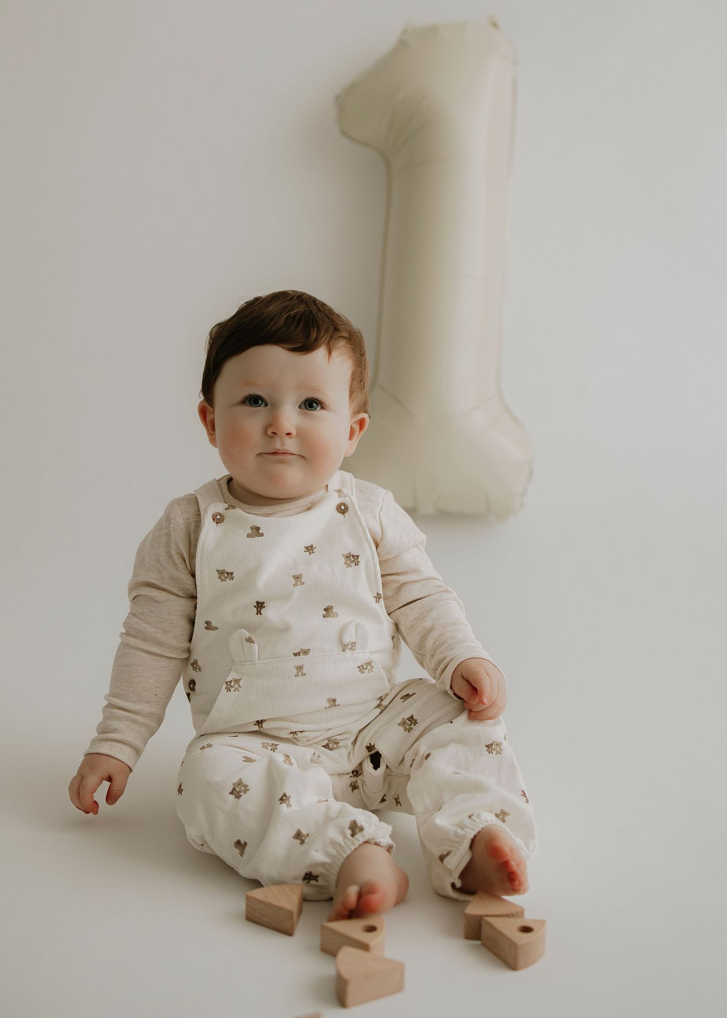 Baby wearing cream floral outfit sits on floor with wooden blocks.