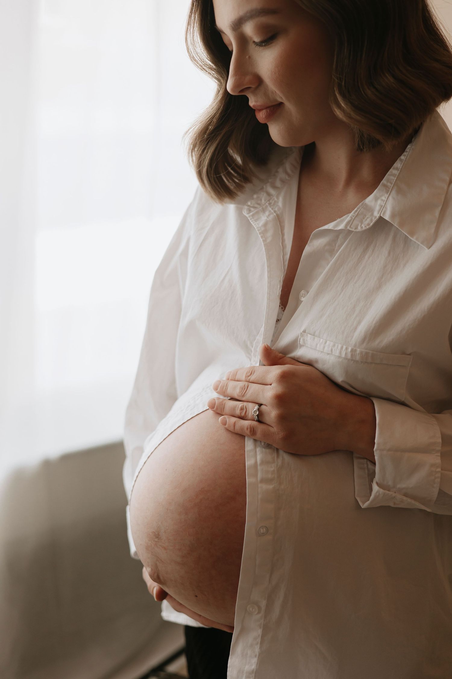 Intimate maternity photography session with soft lighting and white button-down shirt.