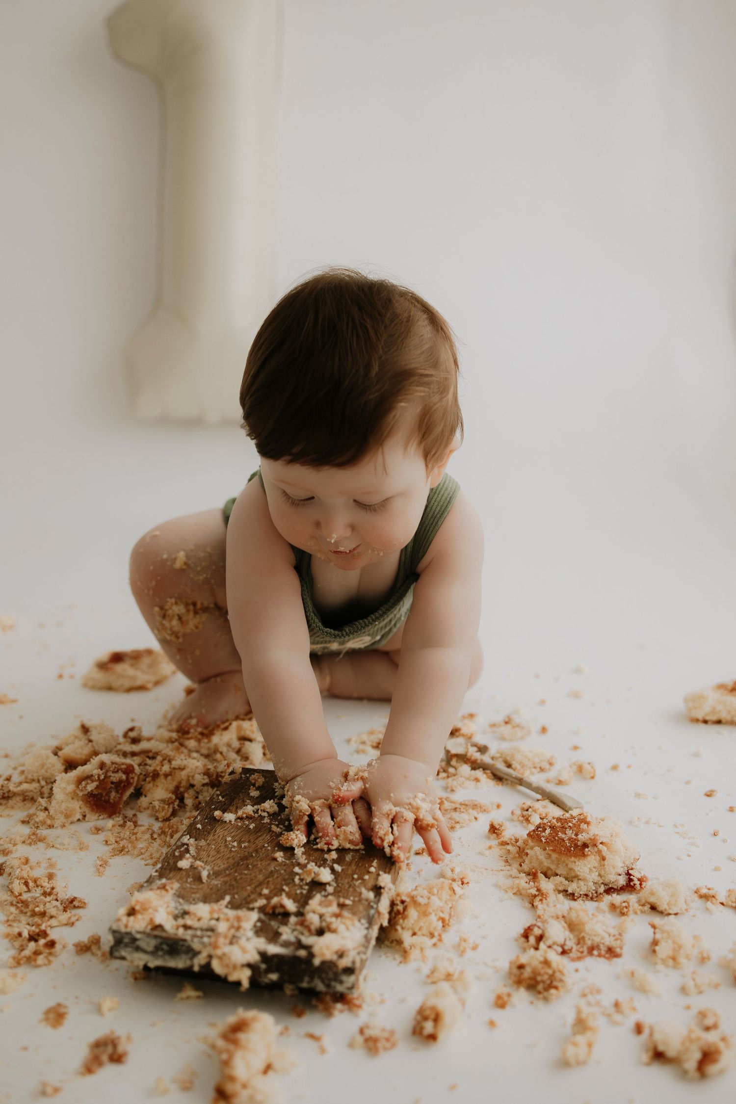 Baby crawling and exploring smashed cake on white floor.
