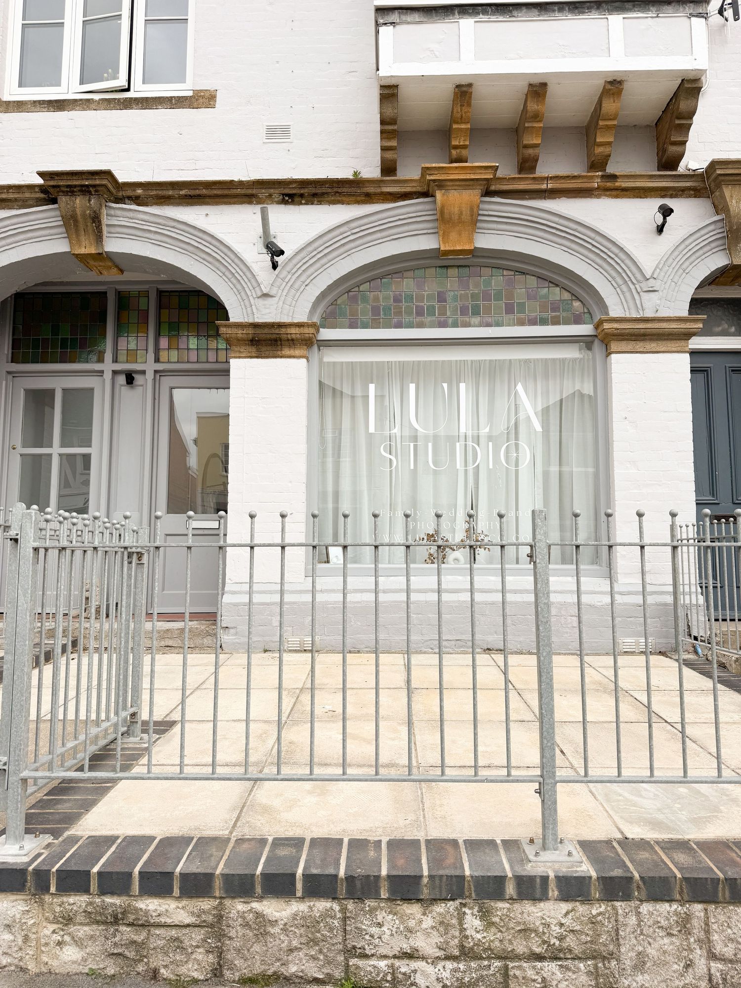 Lula Studio storefront with elegant white arched facade, iron fence, and colorful stained glass windows.