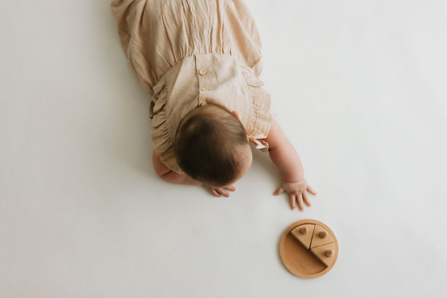 Overhead view of baby lying on cream colored surface.