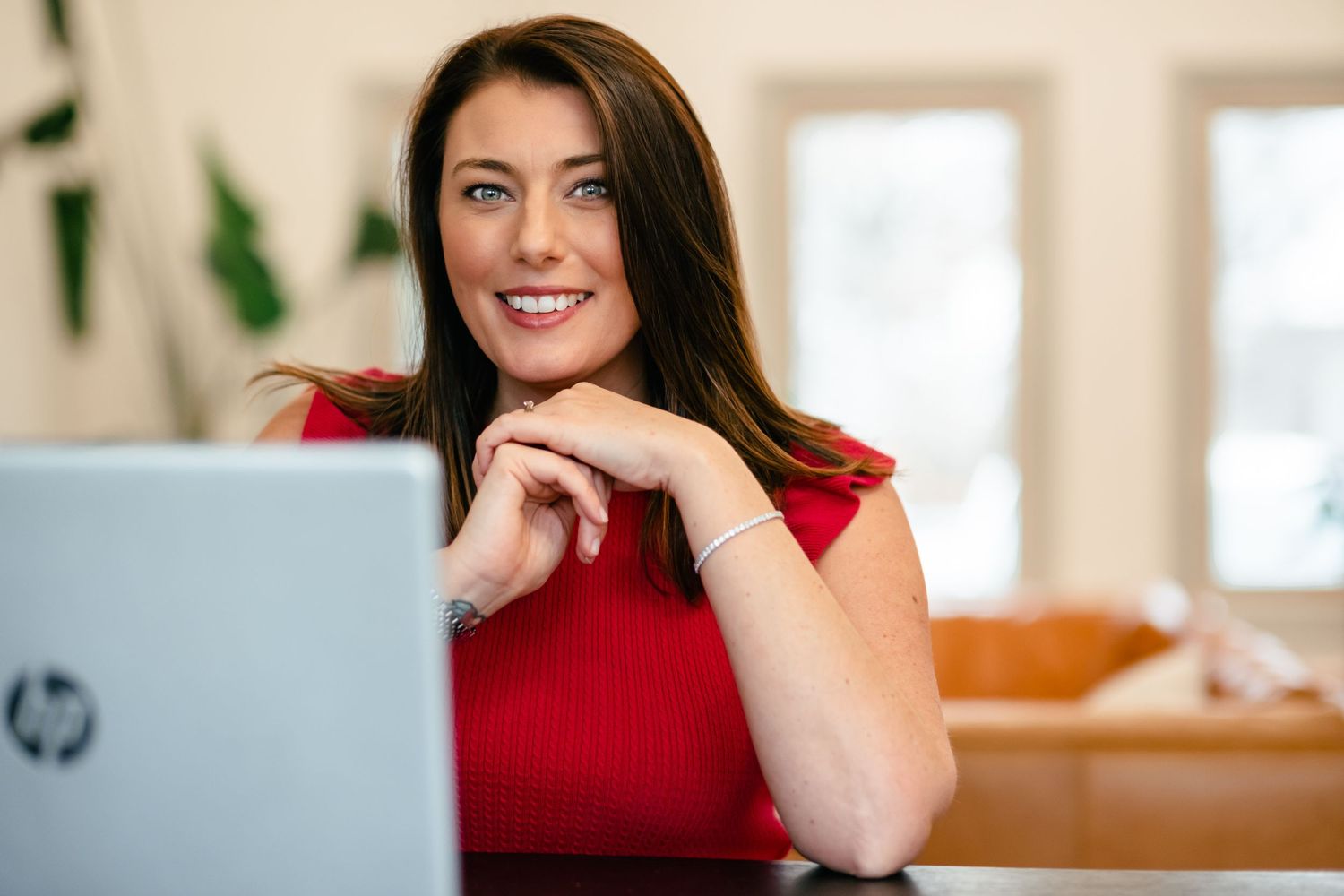 Woman in red top smiling while working on laptop at home desk.