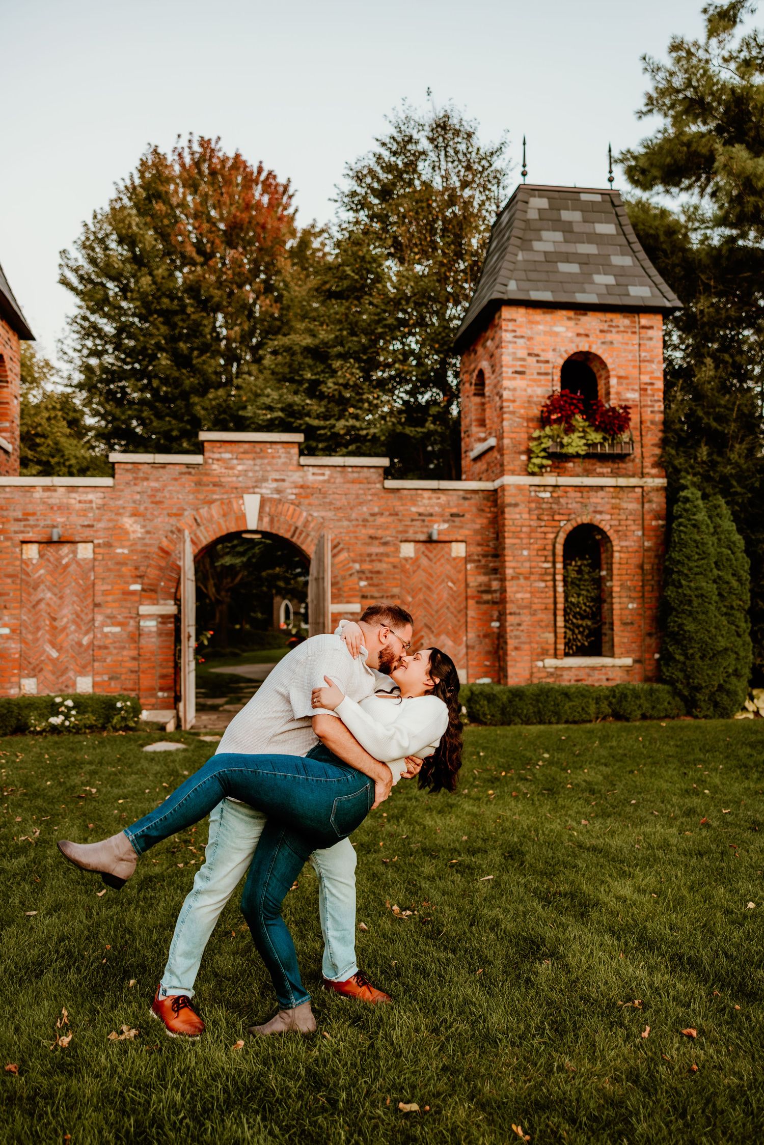 Romantic couple embracing in front of rustic brick wall and tower at sunset.