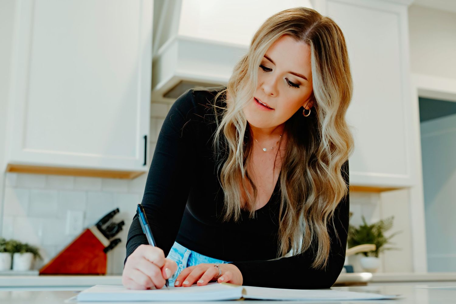 Person writing notes at counter in bright modern kitchen with subway tile backsplash.