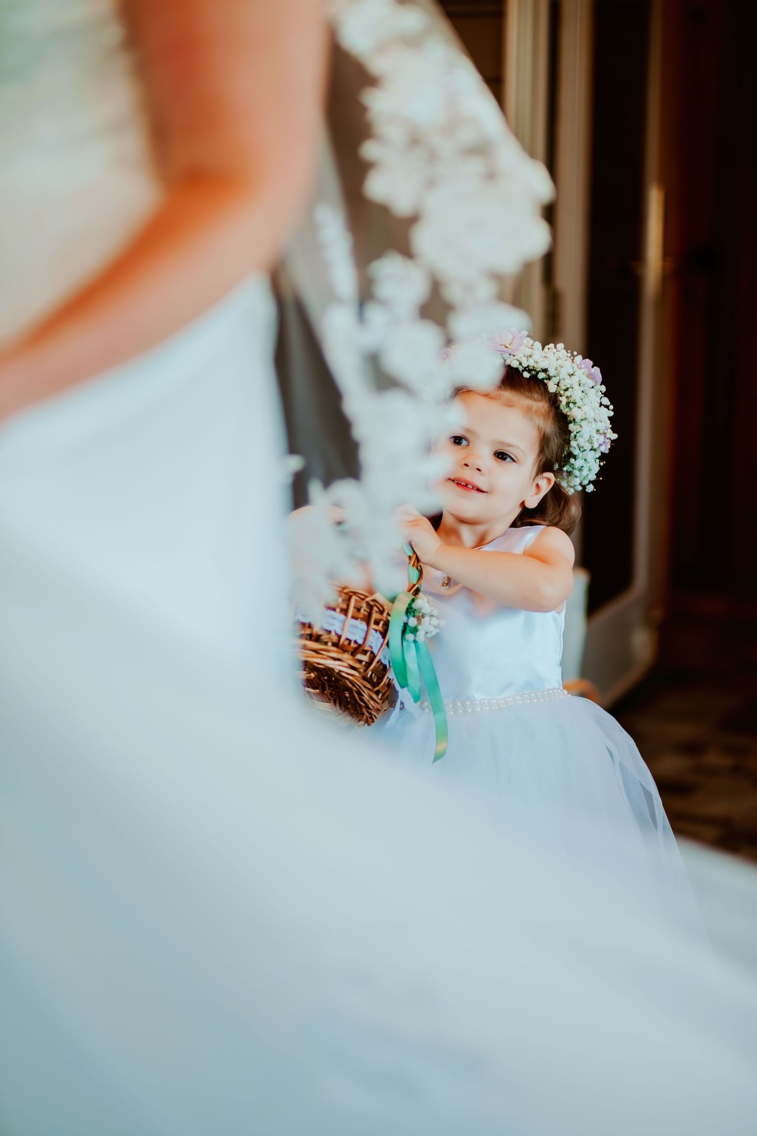 Young flower girl in white dress and floral crown watching the bride.