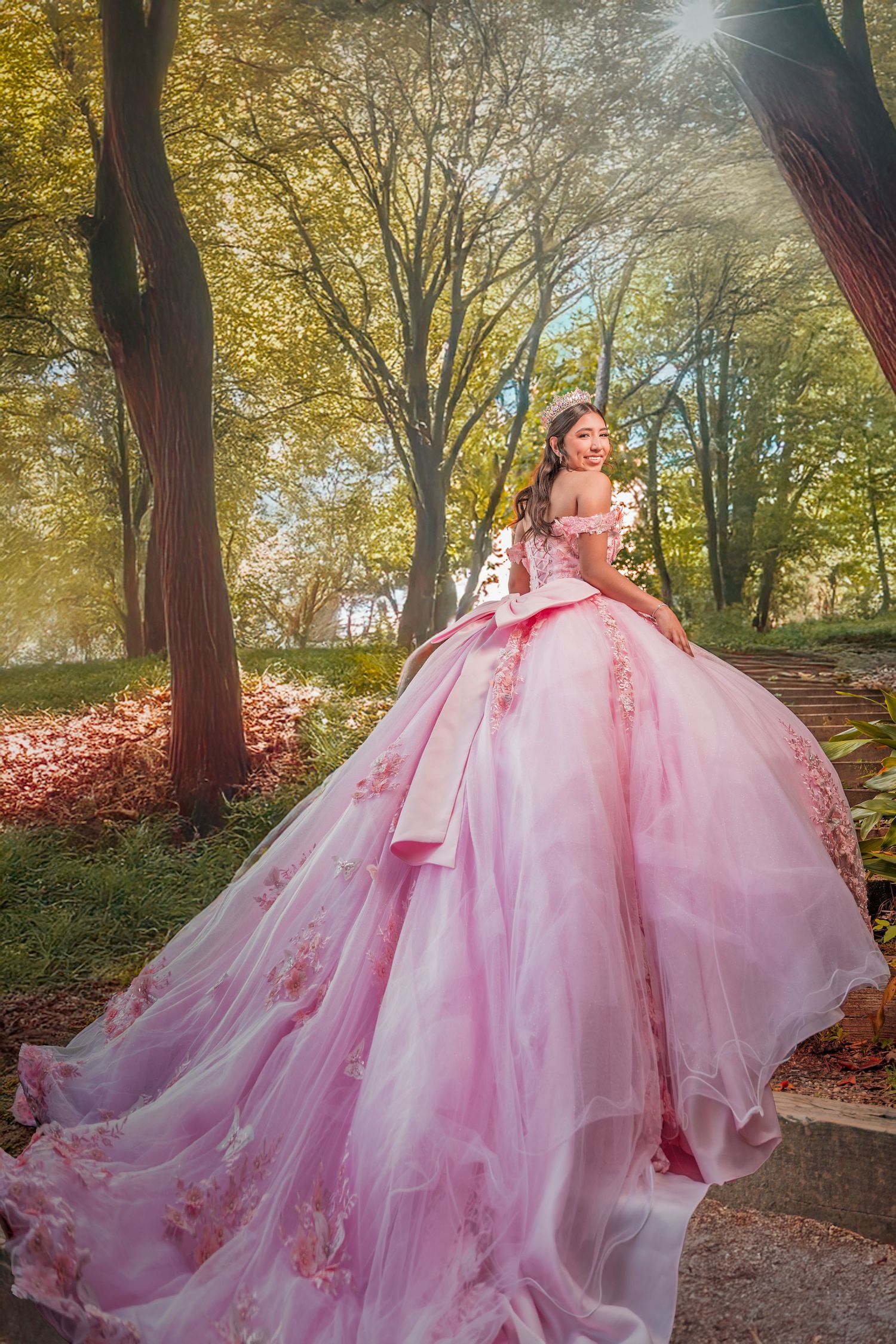 A pink tulle ballgown flows gracefully through a sunlit autumn forest path with golden leaves overhead.