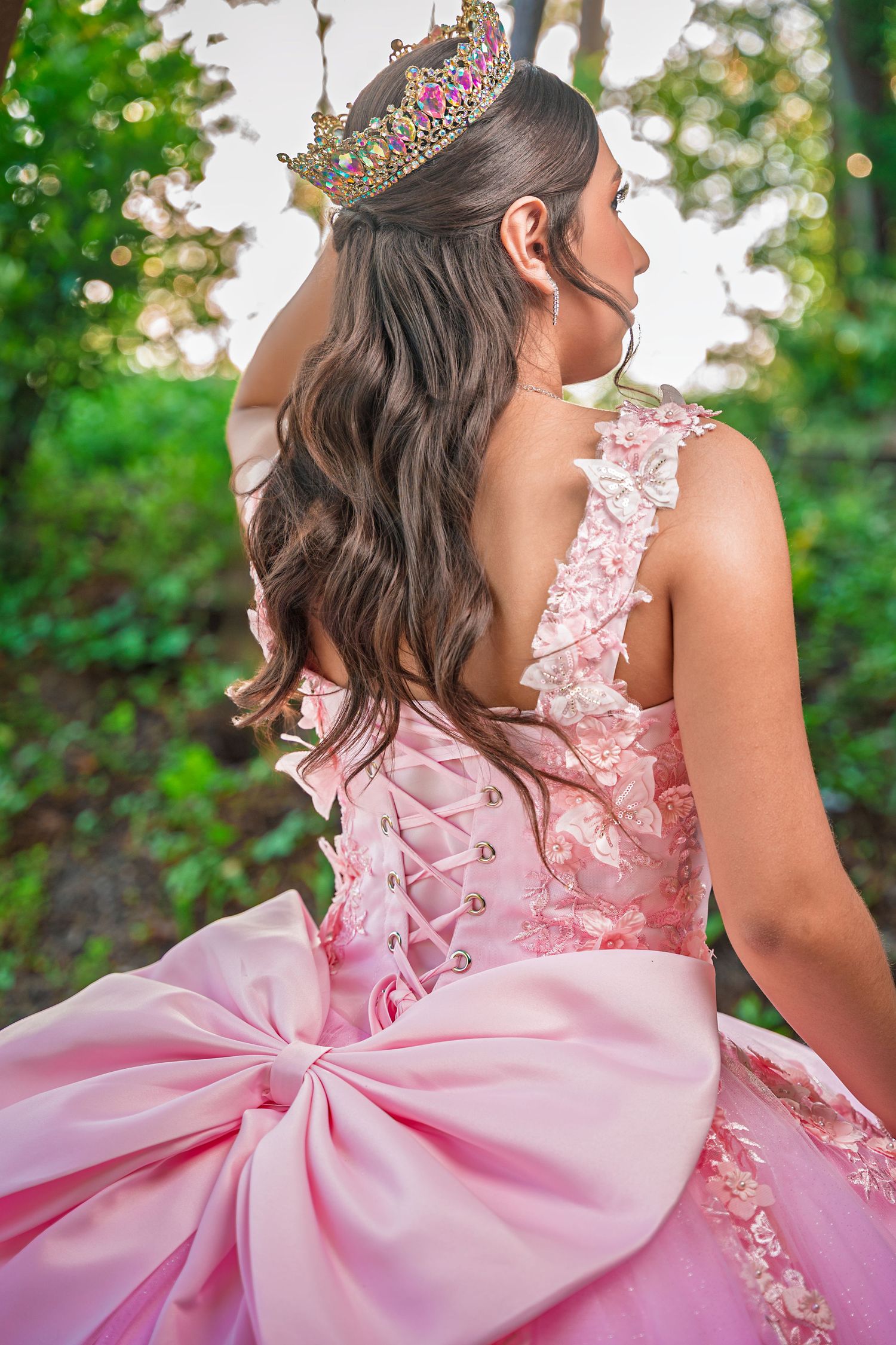 Large pink bow detail on the back of a formal gown with floral lace embellishments captured in a garden setting.