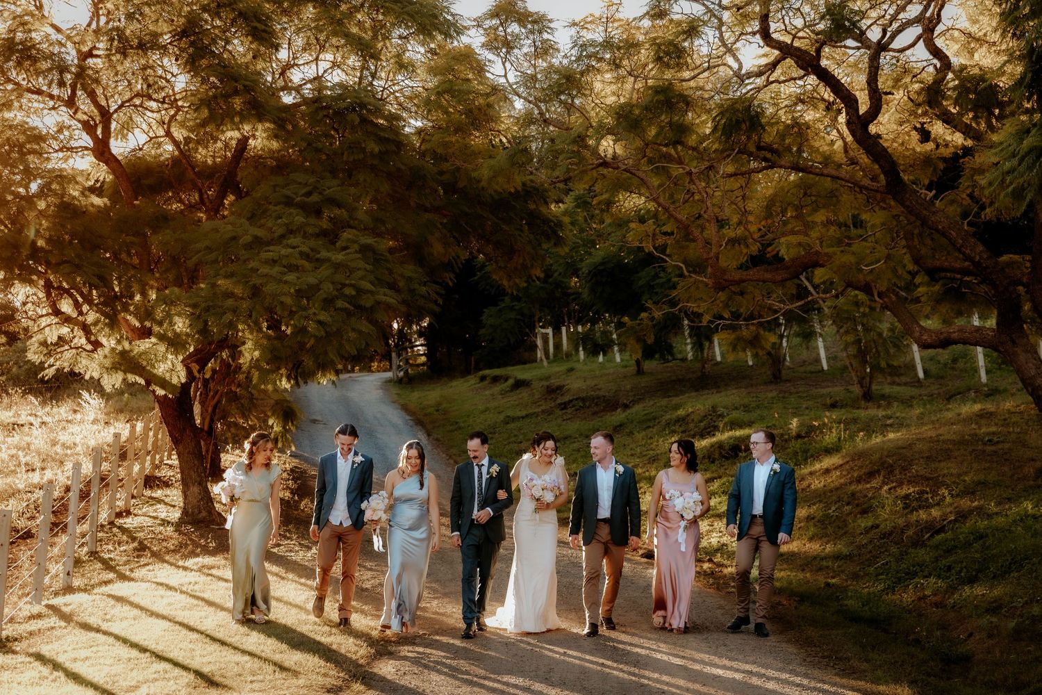 Wedding party lined up under autumn trees in pastel blue and gray attire.