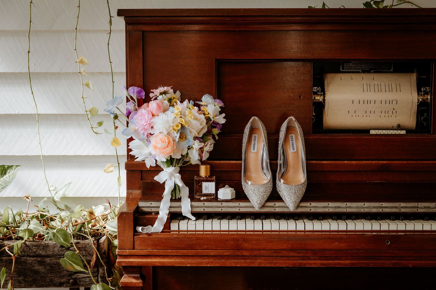 Wedding accessories and shoes arranged on vintage piano with floral decorations.