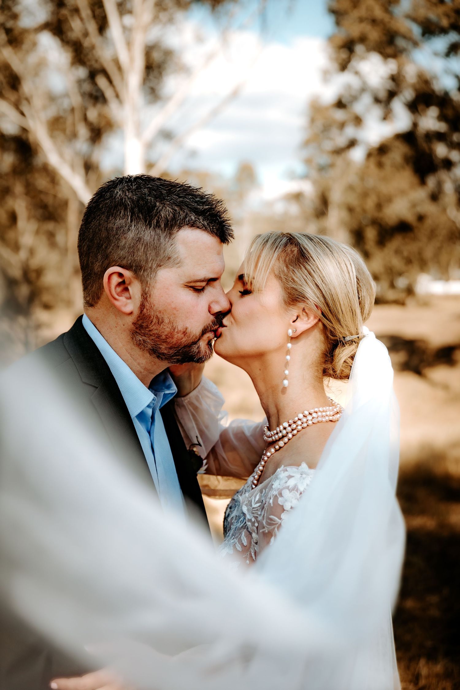 Romantic wedding couple sharing an intimate moment through a white veil in natural lighting.