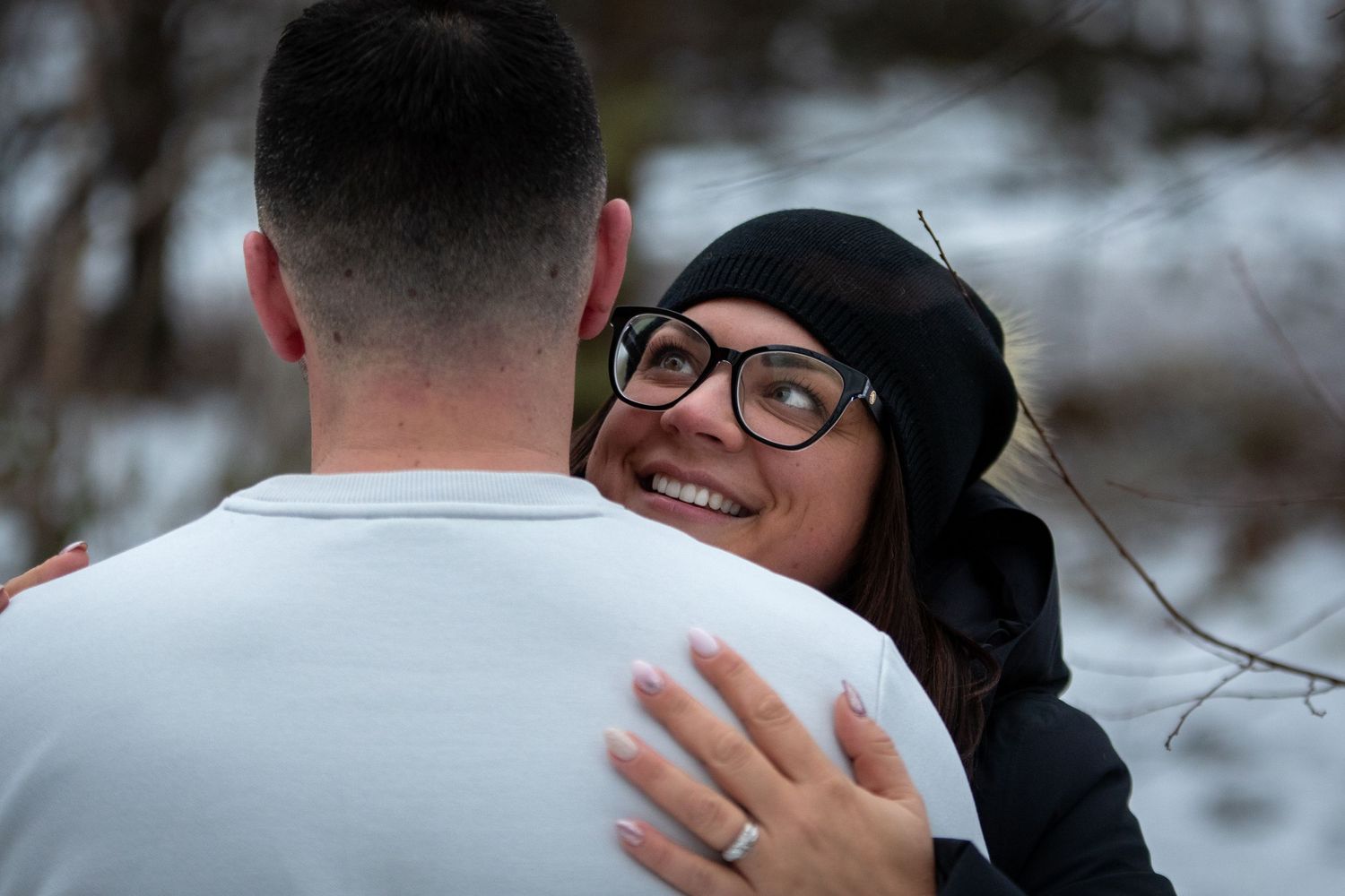 Close-up of embrace between two people during winter, one wearing glasses and beanie.