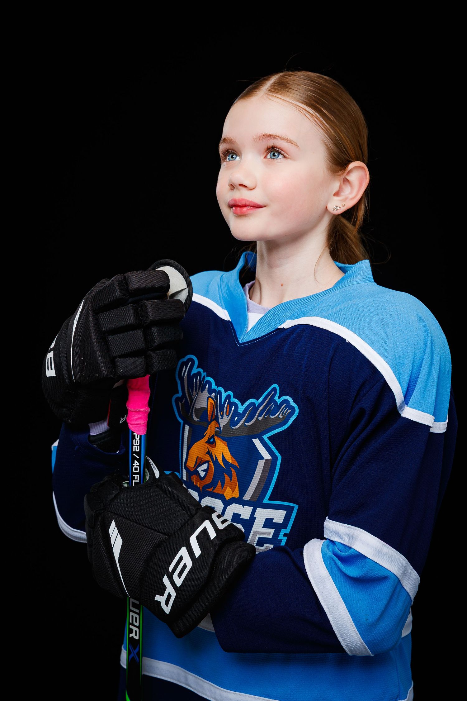 Young hockey player in blue and navy jersey poses against black background in dramatic side profile sports portraits.
