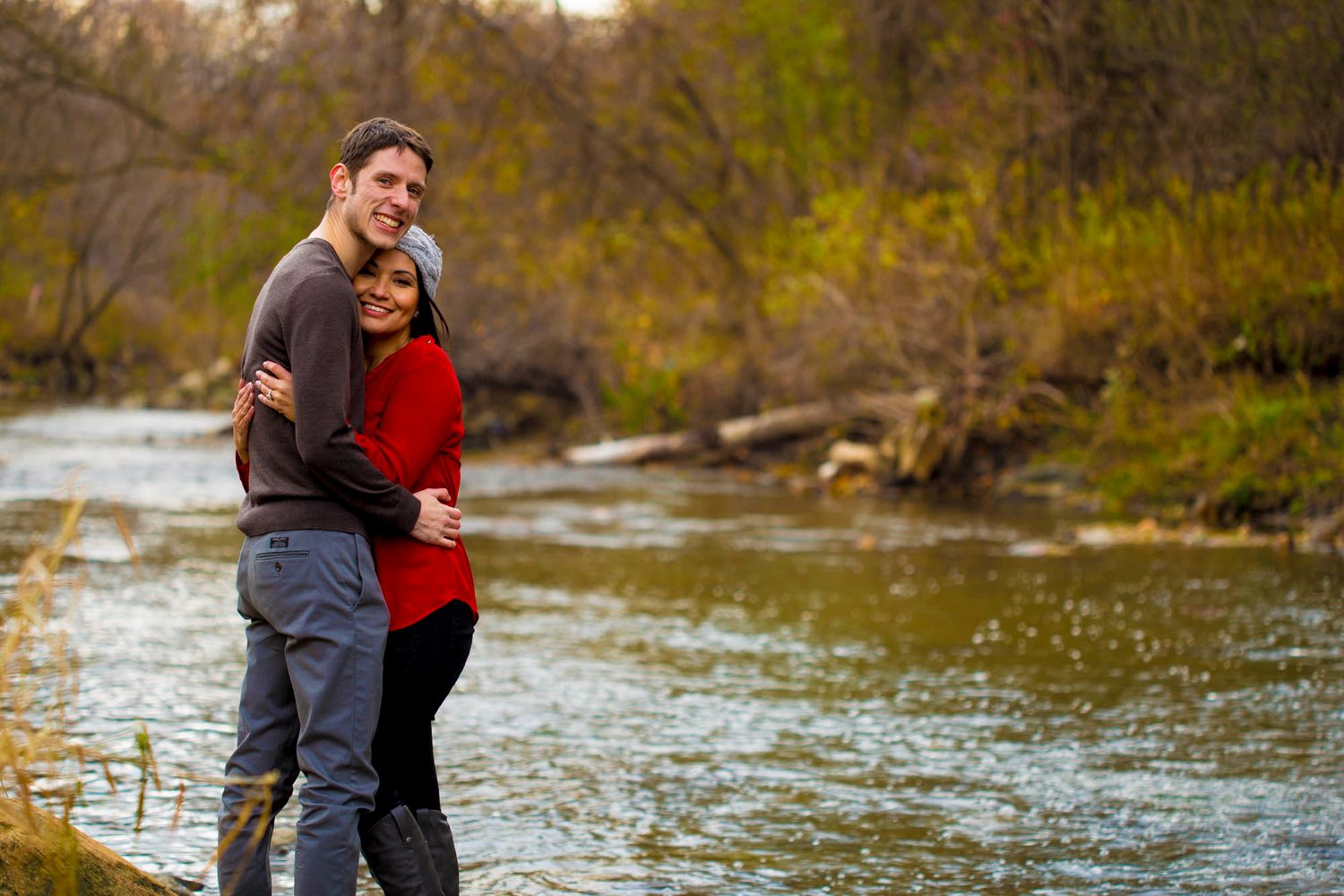 A couple shares a romantic moment together by a flowing river surrounded by autumn foliage.