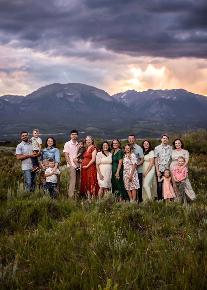 Large family portrait in a mountain meadow at sunset with dramatic cloudy skies in the background.