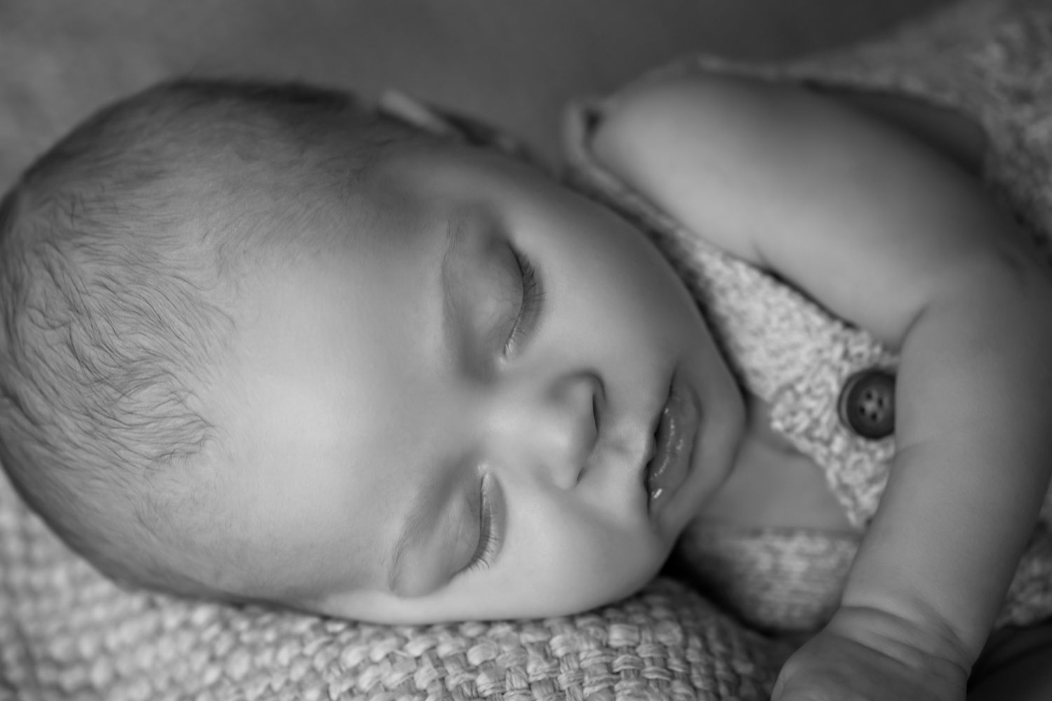 Black and white close-up portrait of a peaceful sleeping newborn baby resting on a soft textured blanket.