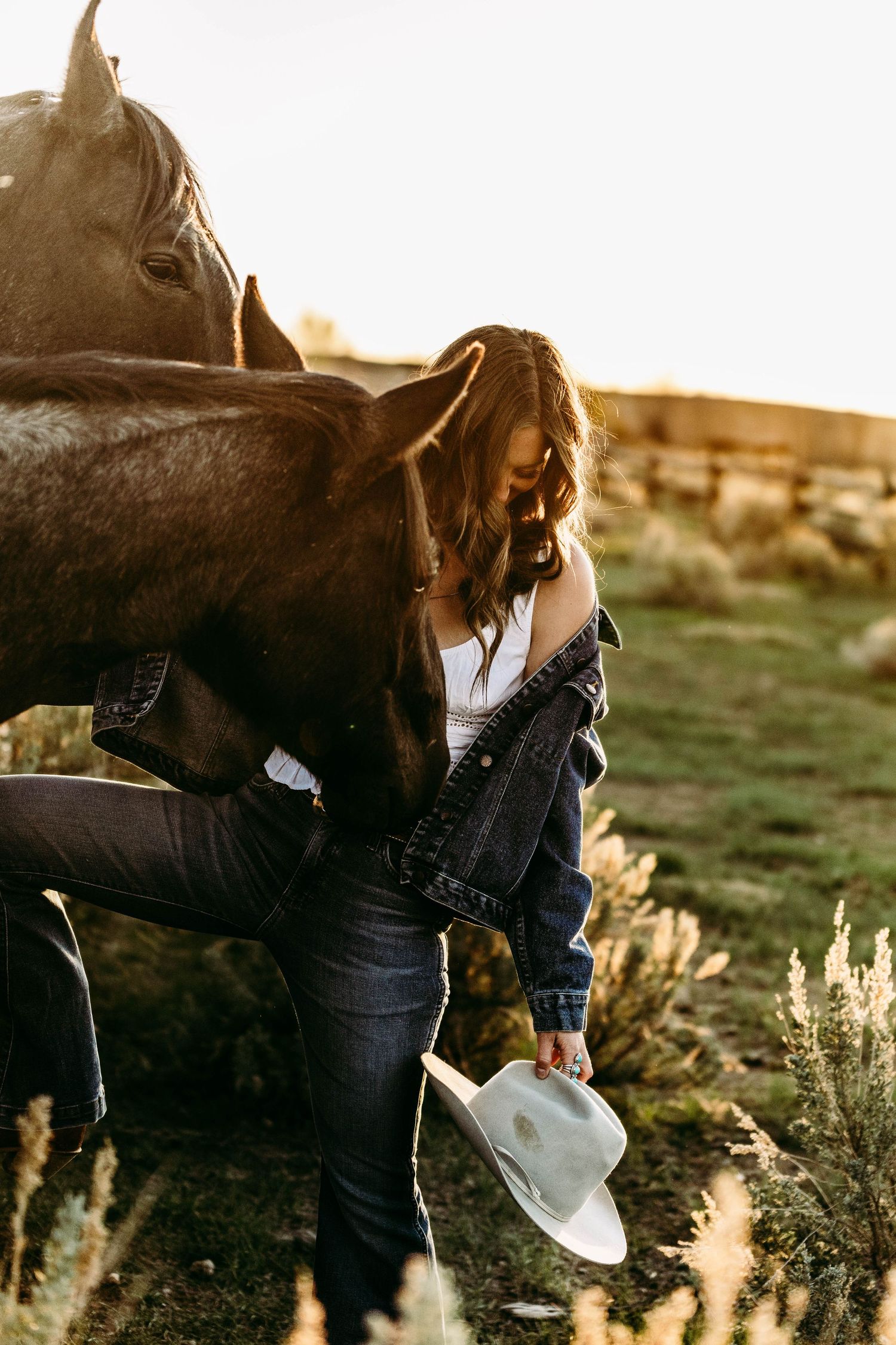 Horse and rider in denim stand together at sunset in a rural field setting.