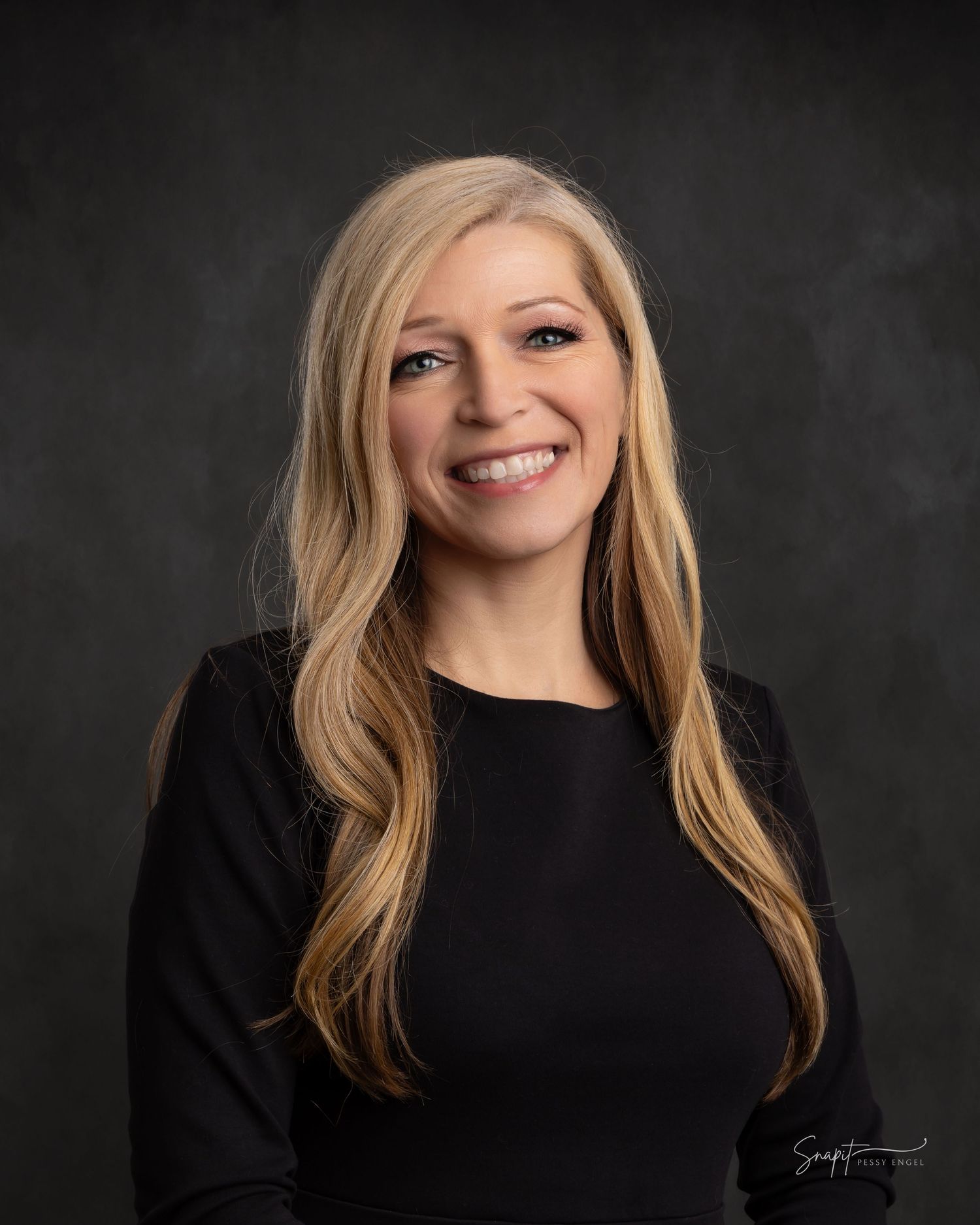 Professional headshot of smiling blonde woman in black top against dark studio background.