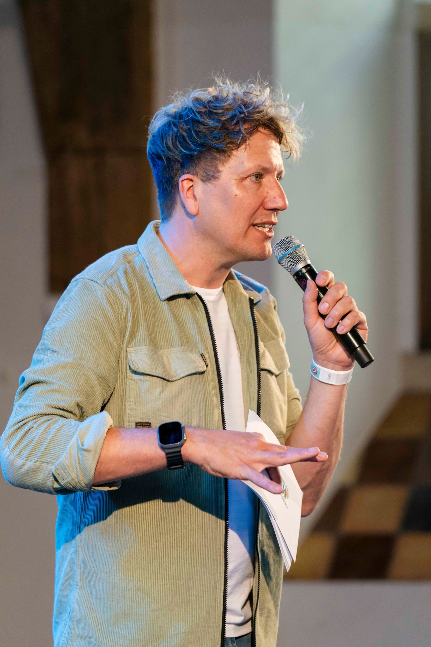 A performer in casual attire speaks into a microphone on stage.