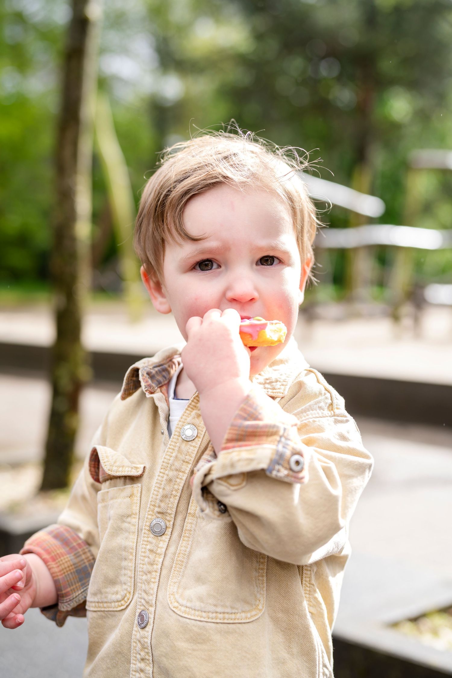 Young child in a tan jacket enjoying a snack outdoors.