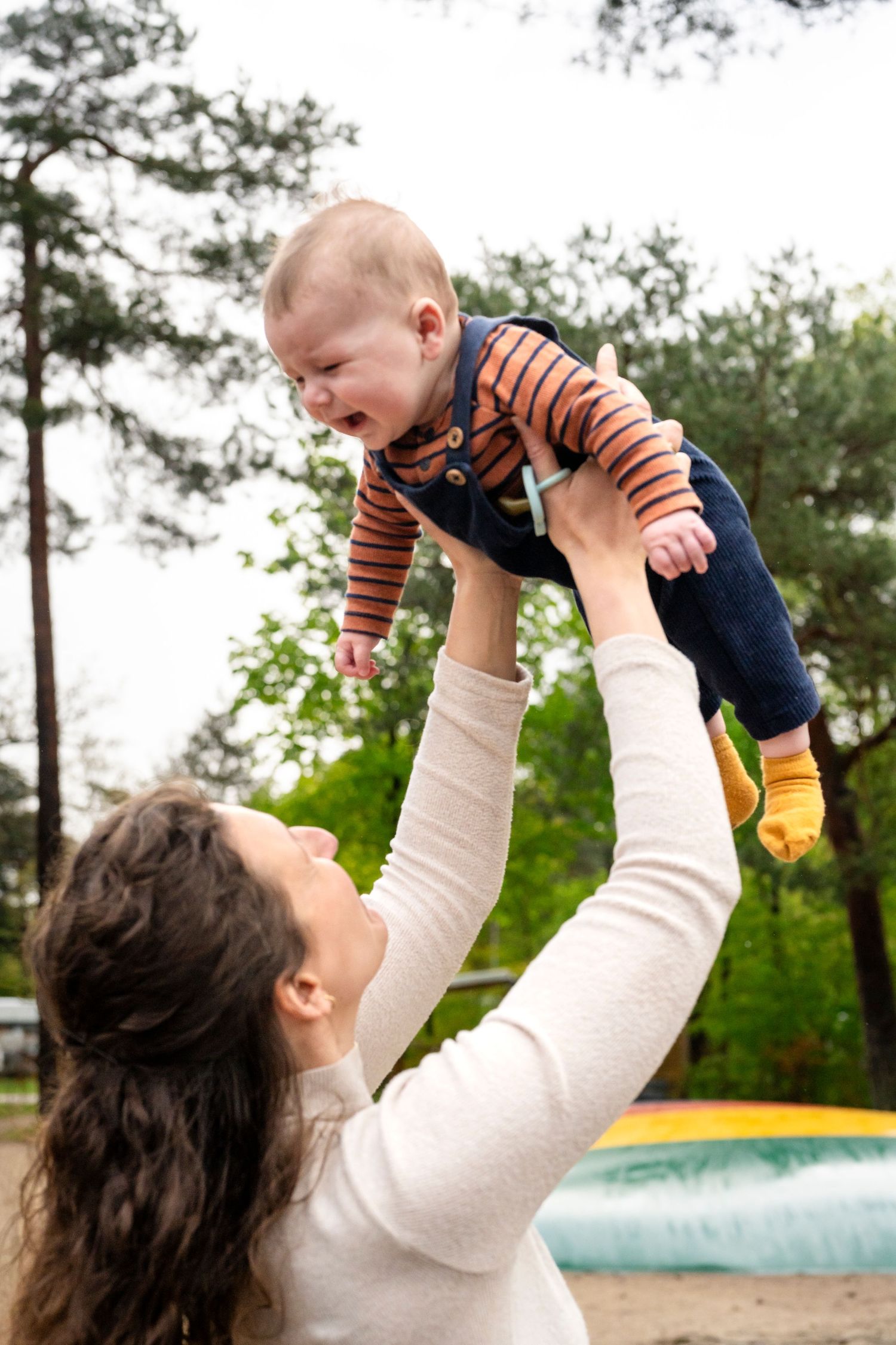 Parent lifting and playing with baby in outdoor park setting.