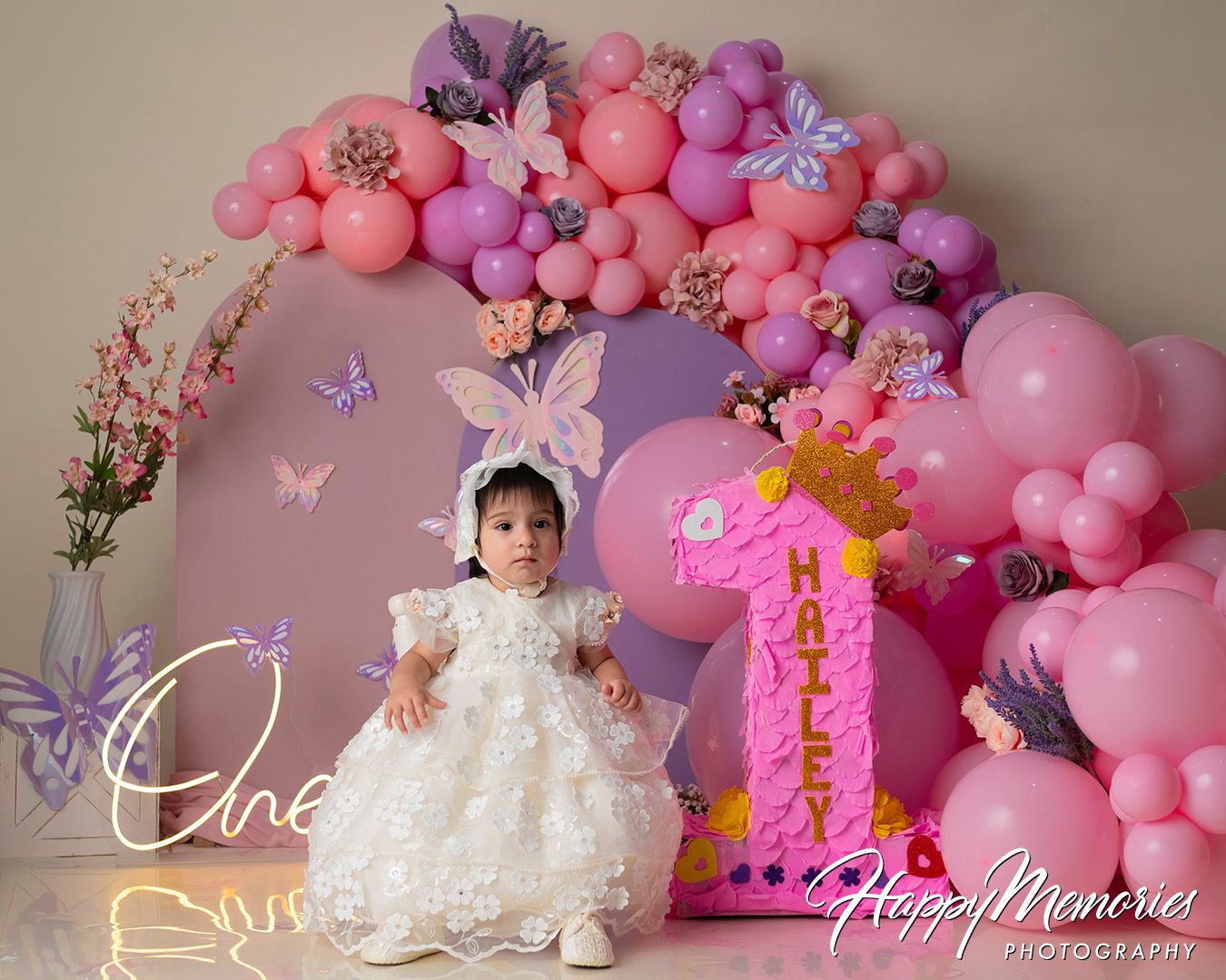 Pink and purple balloon arch with butterflies decorates a first birthday celebration setup with a number one display.