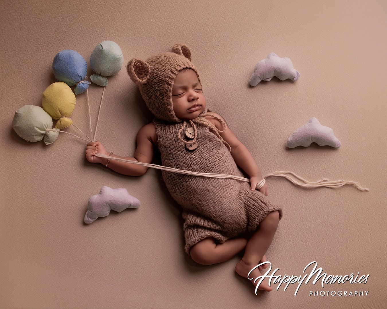 A newborn baby sleeping peacefully on a soft pink backdrop with delicate white clouds and plush toys.