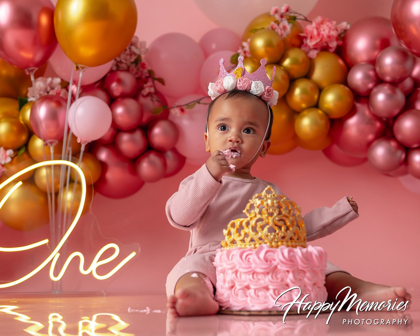 Pink and gold balloon arch creates a festive backdrop for a first birthday cake smash photo session.