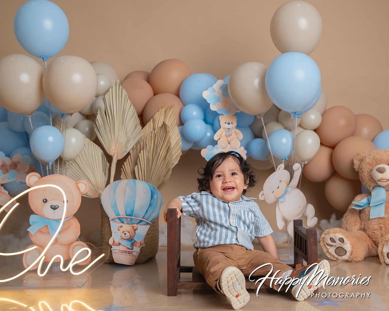 Baby boy cake smash photo session with blue and beige balloons and rustic wooden decorations.
