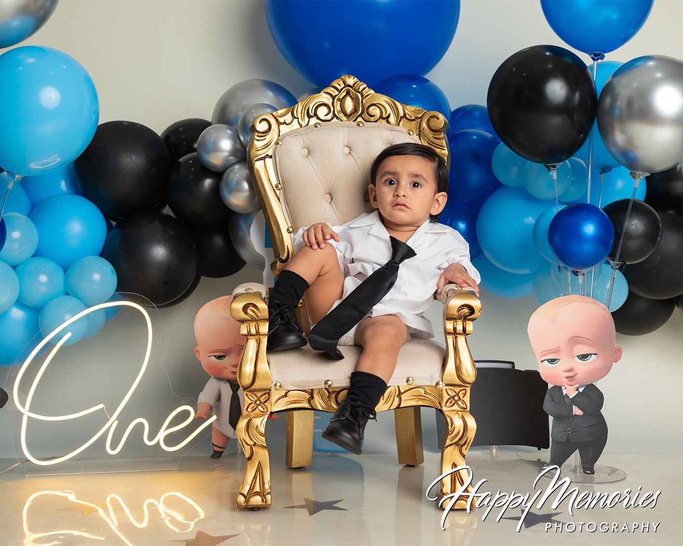 A festive balloon garland in blue, black, and silver colors decorates a party setup with gold accents and decorative elements.