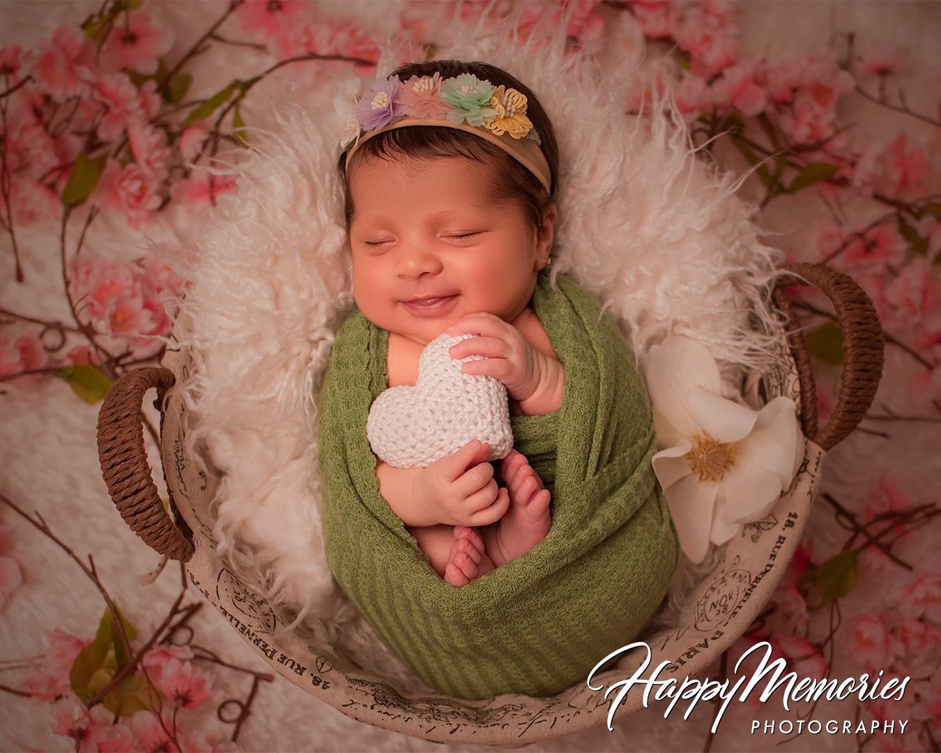 Newborn photography series with white floral decorations and soft green wrapping on a pink backdrop.