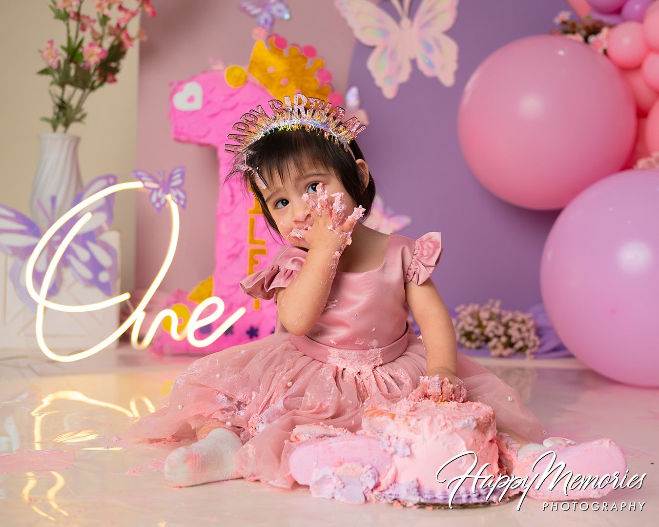 Pink and purple themed first birthday party setup with balloons, butterflies and floral decorations.