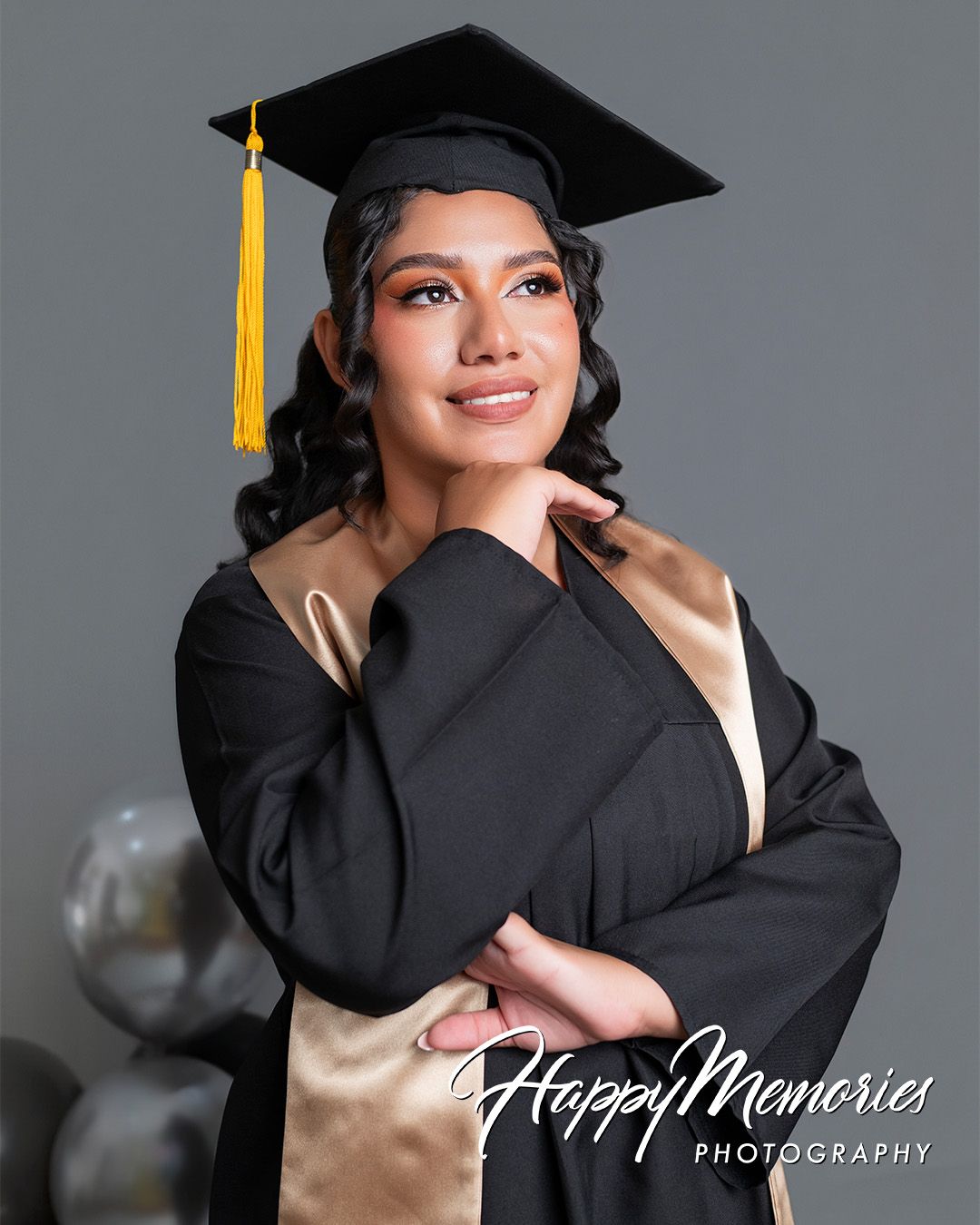 Graduation portrait series in black cap and gown against grey studio background.