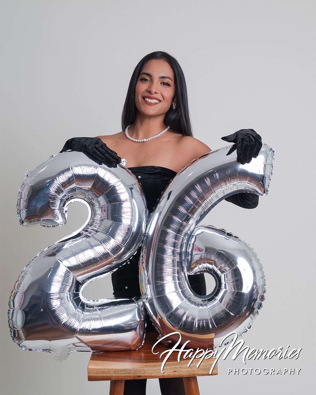 Woman holding silver number balloons spelling 2025 against white background.