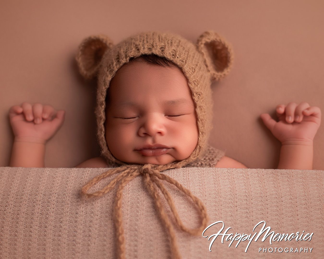 Sweet sleeping newborn wearing teddy bear bonnet in soft natural lighting.