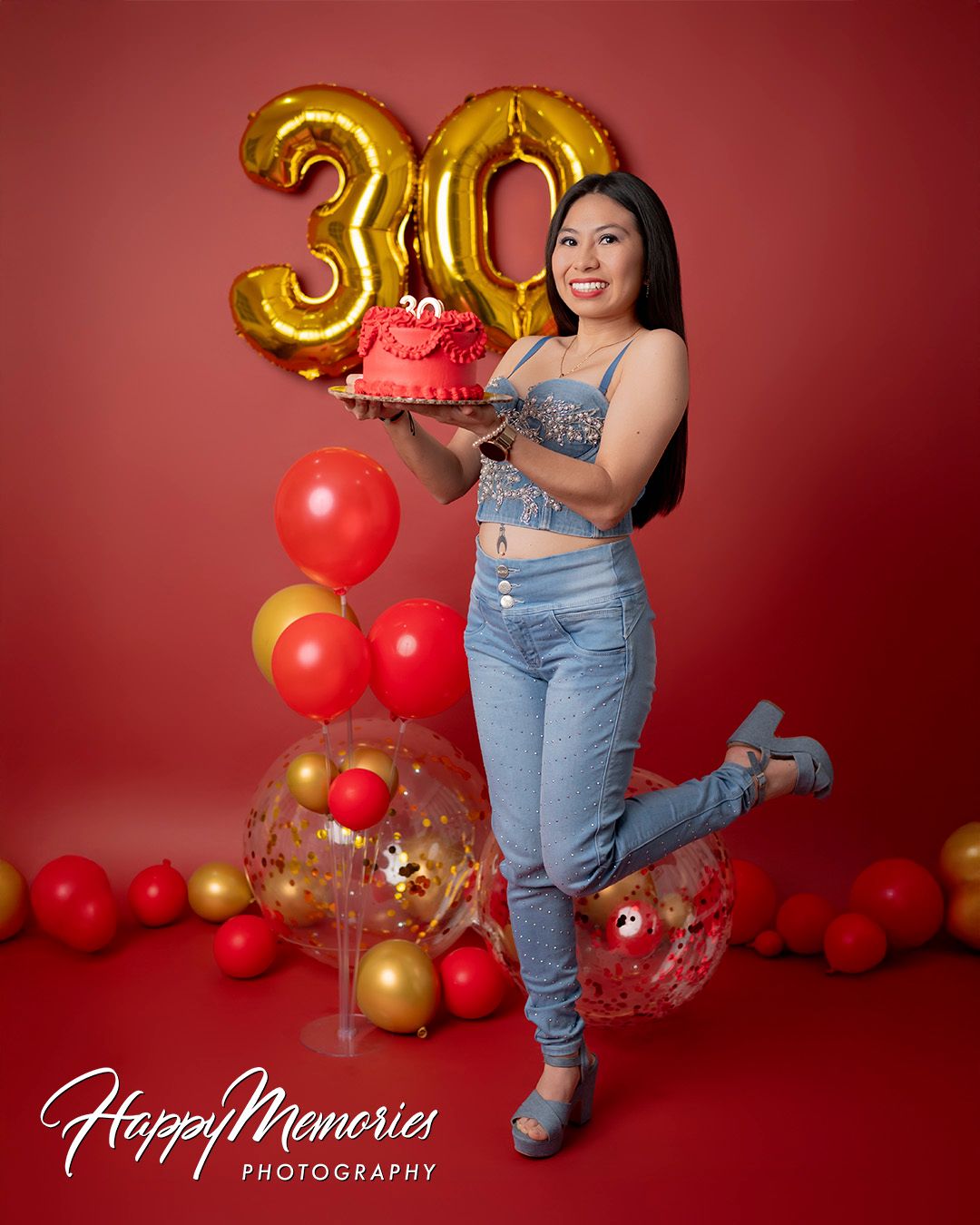 Celebratory photos with number balloons and casual denim outfit against red backdrop.