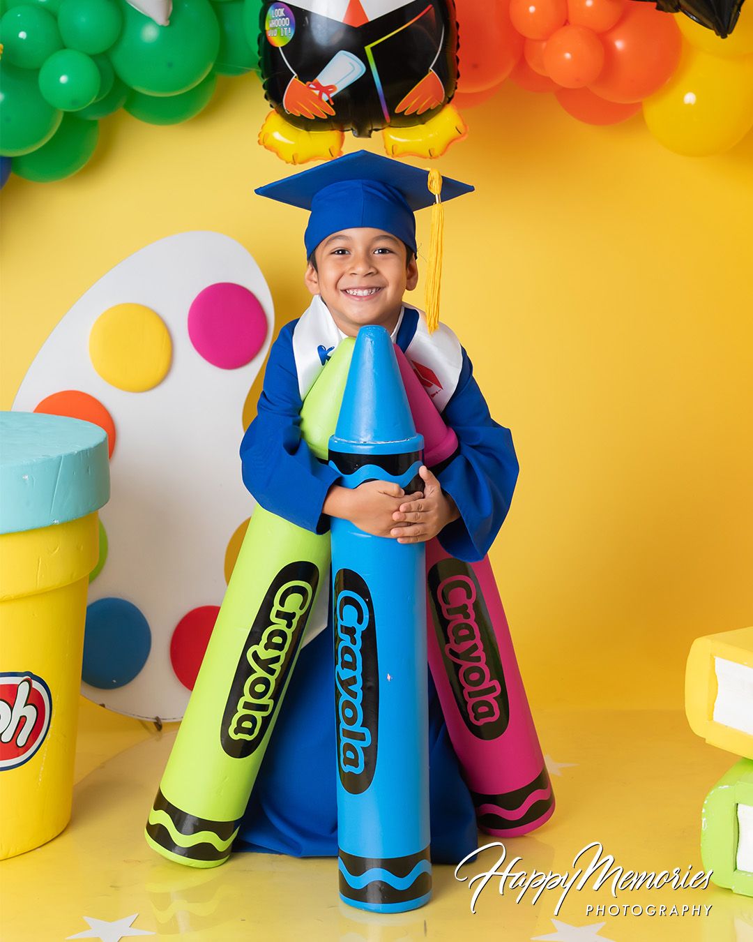 Colorful graduation photo display with giant crayons and rainbow balloon decorations.