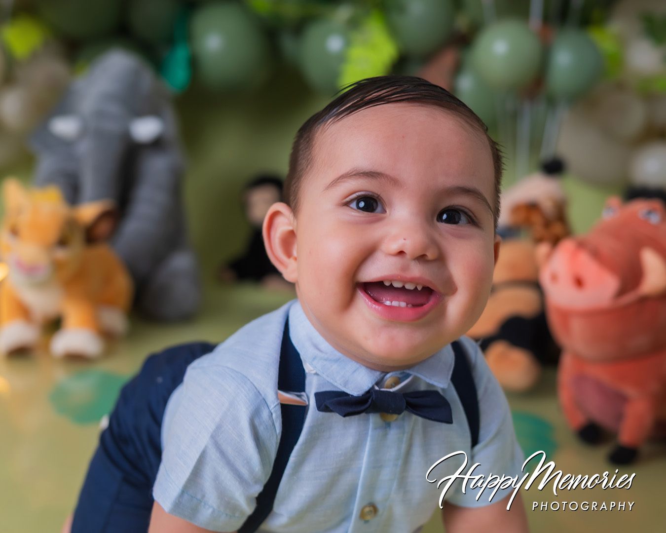 A smiling child wearing a navy blue bow tie and light colored shirt poses for a portrait with toys in the background.