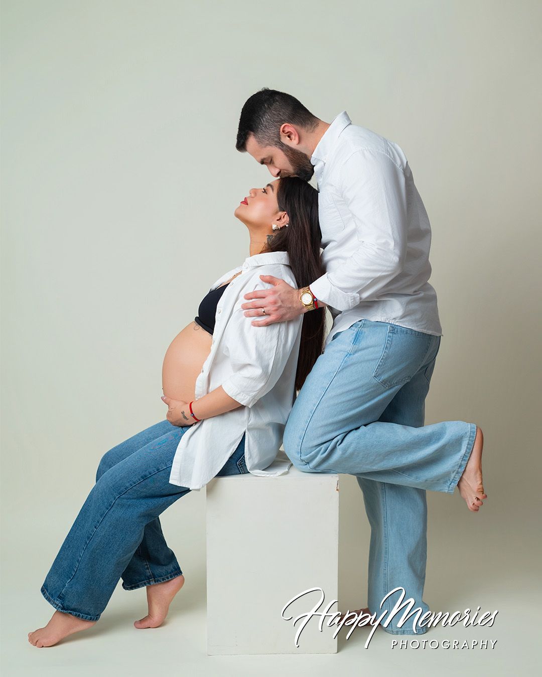 Intimate maternity studio portrait with couple in casual white and denim outfits.