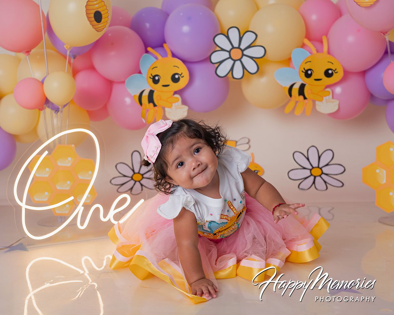Colorful balloon arch with pastel pink, purple and yellow balloons decorated with daisy flowers and bee accents for a party.