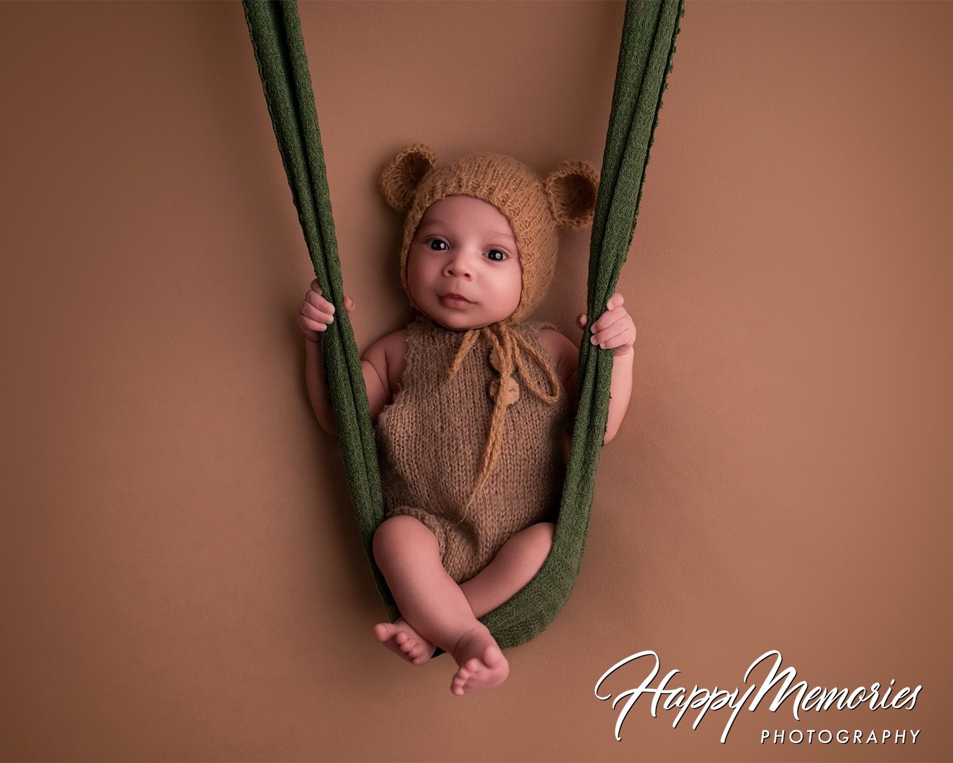 Newborn photography series with baby in brown knit outfit on green swing prop.