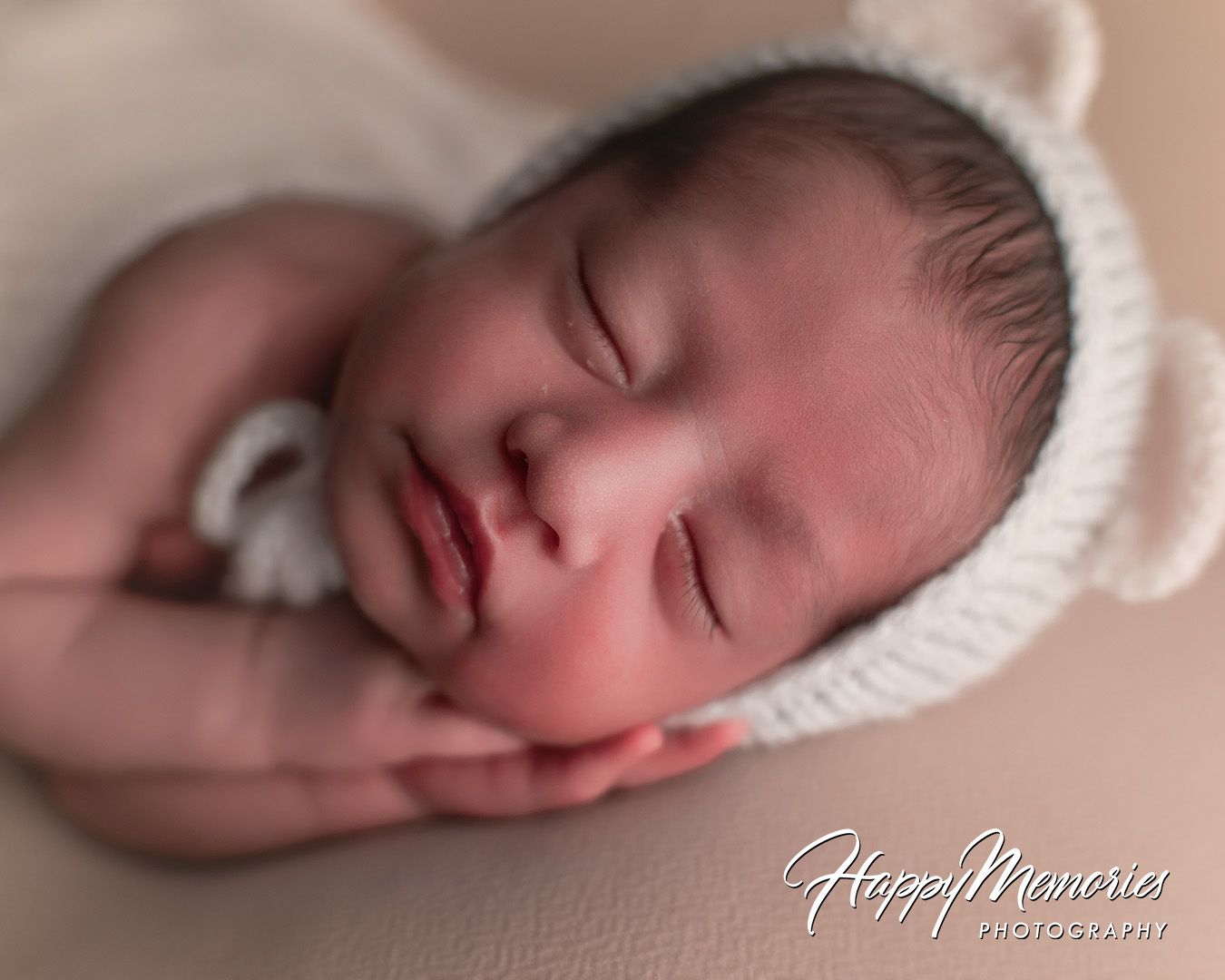 A sleeping newborn baby in soft beige tones lies peacefully wrapped in white blankets.