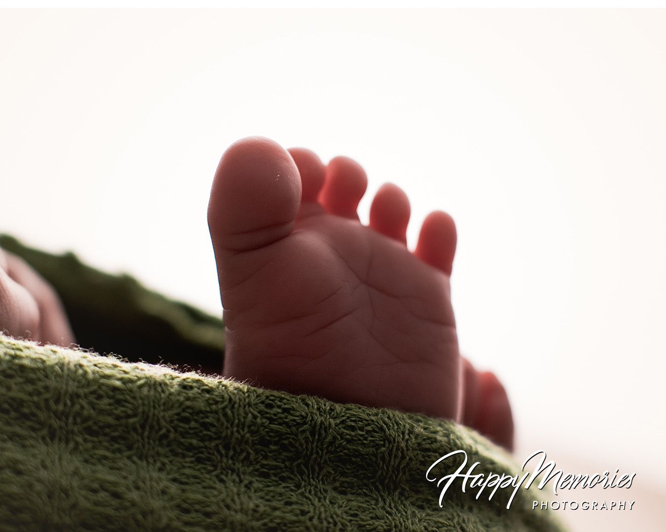 Close-up photograph of a tiny baby's foot resting on green fabric with soft lighting and shallow depth of field.