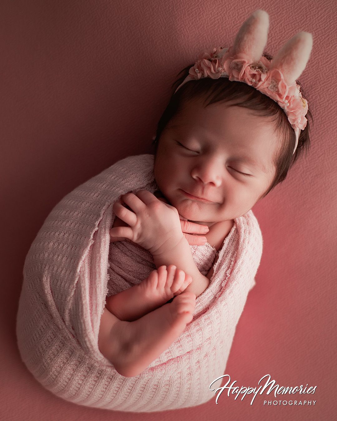 Newborn photography series in soft pink tones showing a sleeping baby wrapped in white knit blanket.
